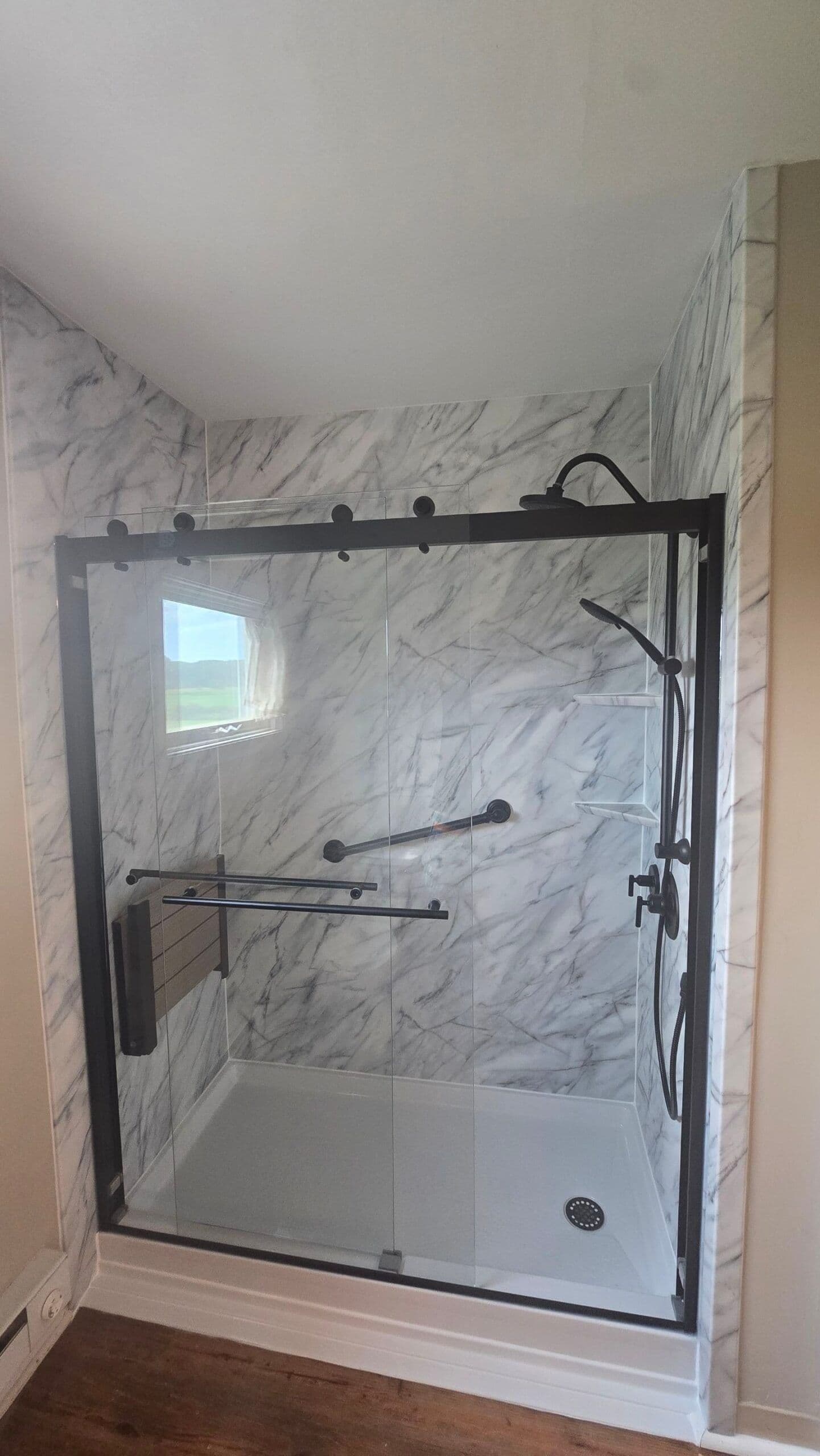 A walk-in shower with sliding glass doors, black fixtures, grab bar, and folding bench seat.