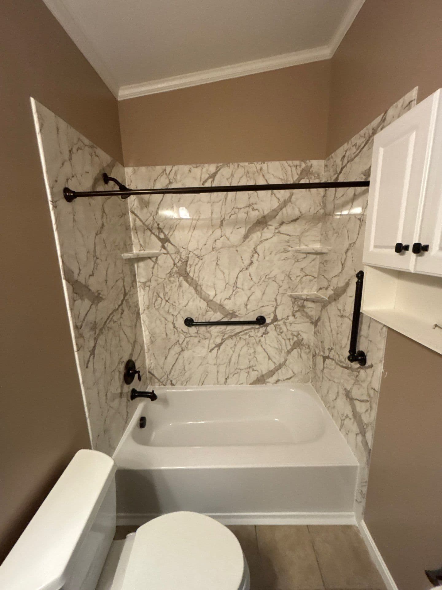 A beige bathroom with a combination shower tub with marbled walls, black fixtures, and corner shelves.