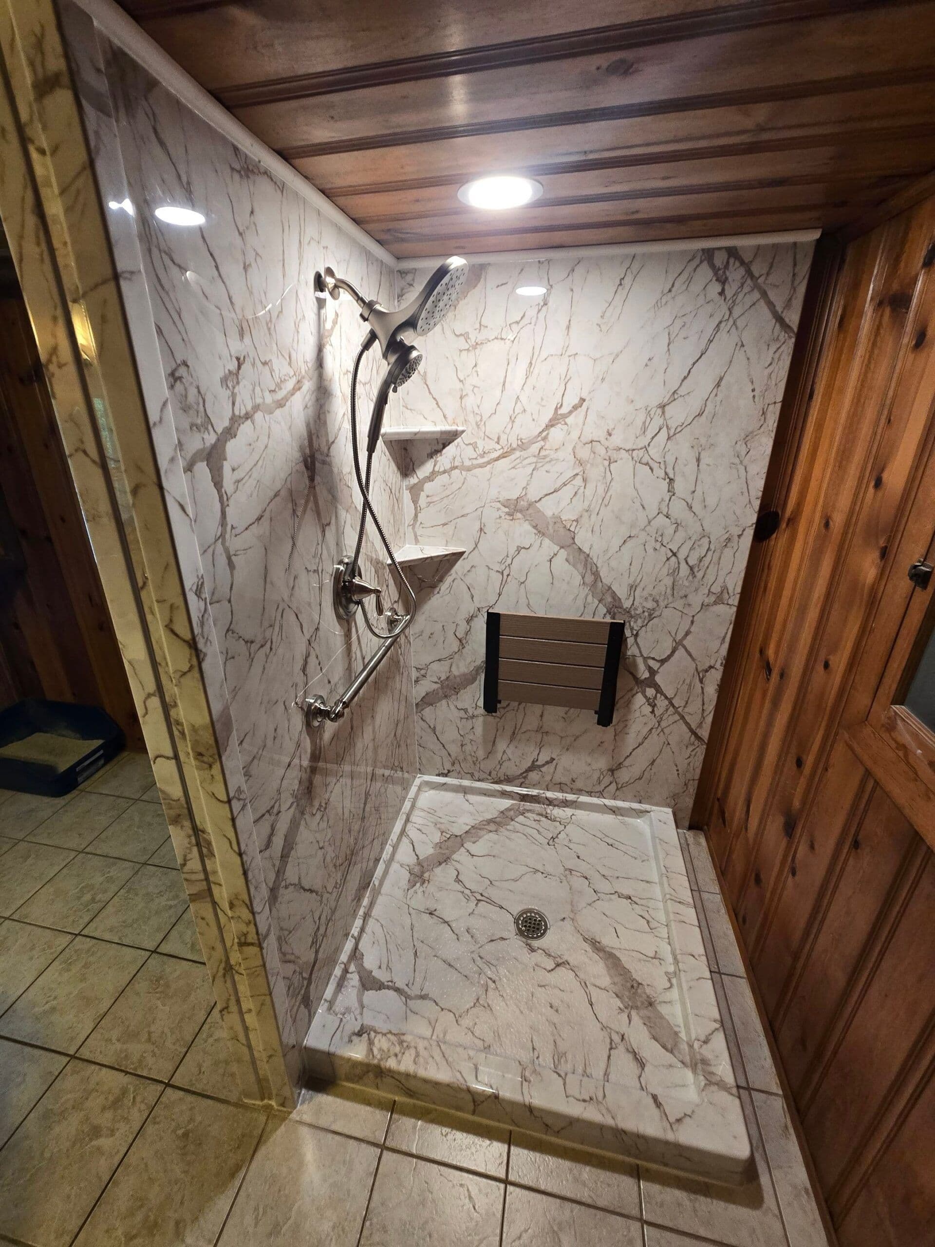 A walk-in shower with folding bench seat, marbled walls, and corner shelves.